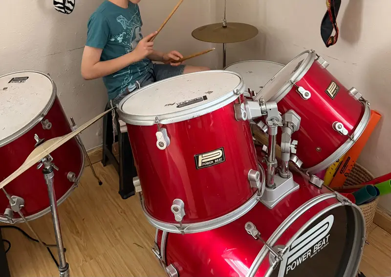 A teenager playing a red drum kit in the music room