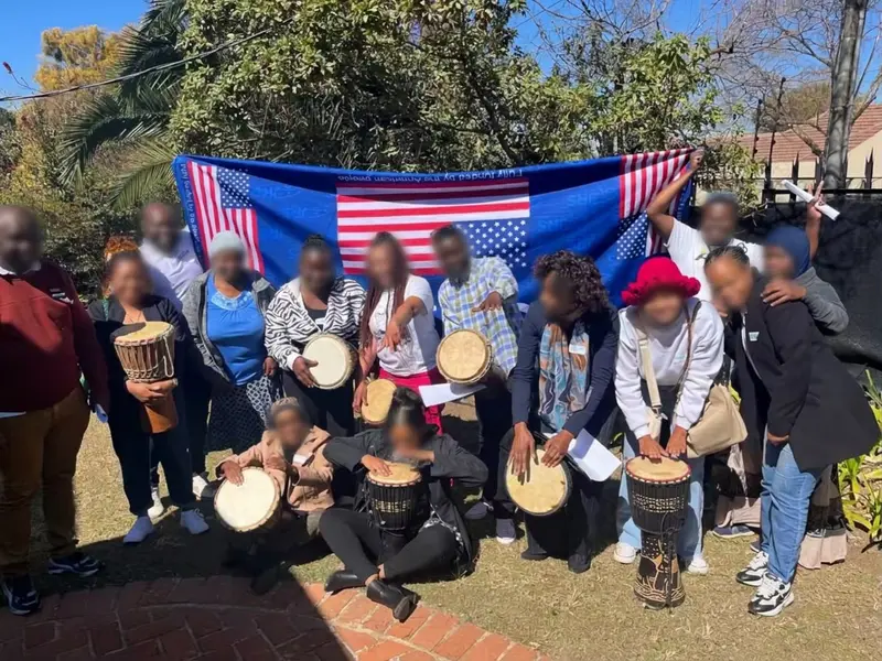A community group drumming workshop outdoors with djembes, led by Yael